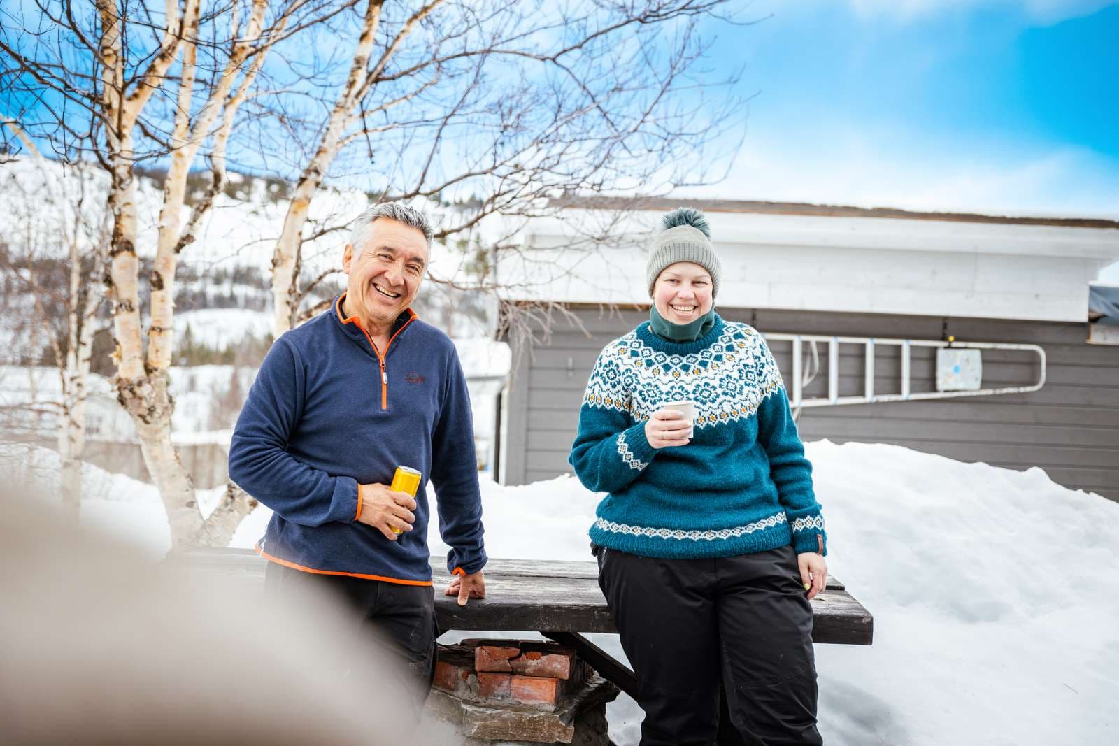 Vinterbild från Beitostölen med två personer som står och fikar utomhus med kaffe och läsk i handen.