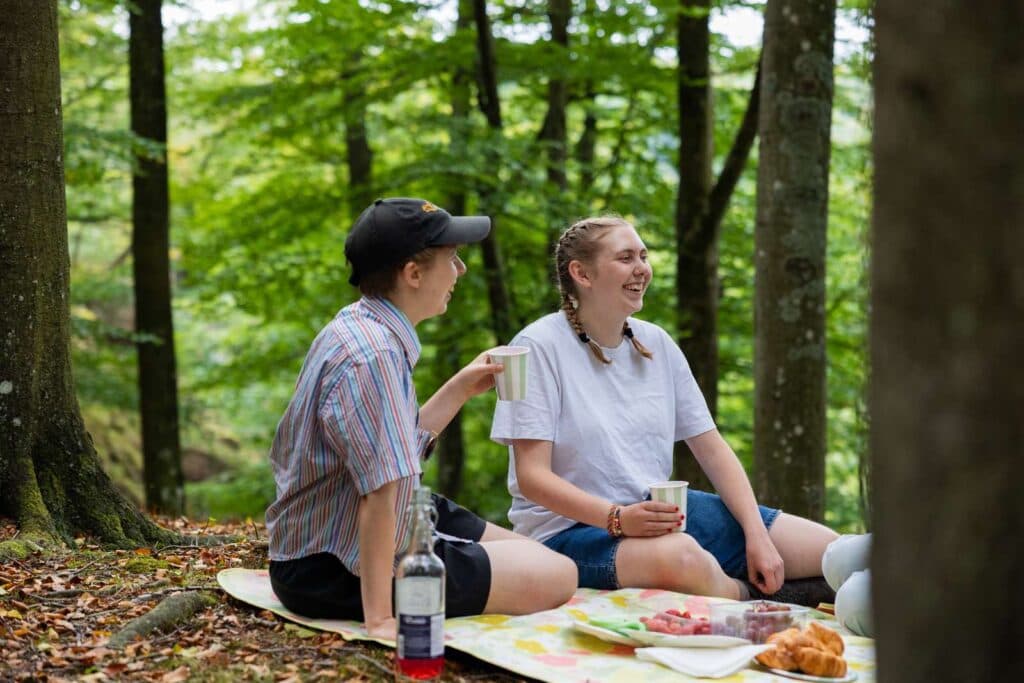 Två personer som fikar i skogen på en picknickfilt.