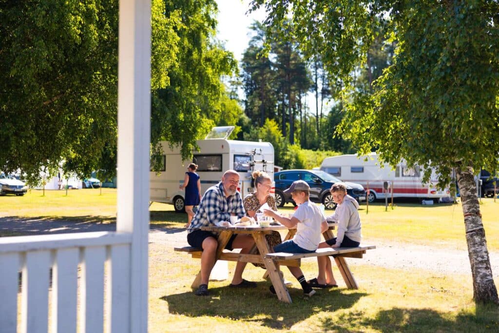 Familj som sitter och äter frukost utomhus utanför stuga på Skara Sommarland camping