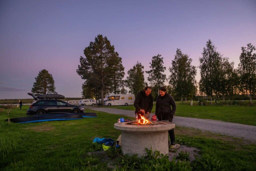 En fin höstkväll där ett par som står och grillar över öppen eld på campingområdet.